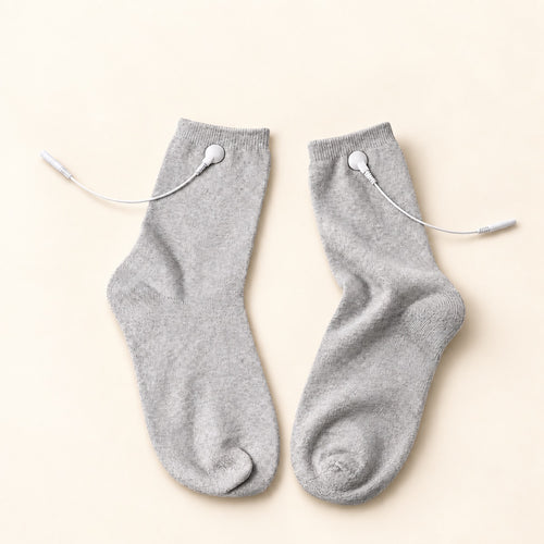 TENS electrode socks with white cables on warm ivory background